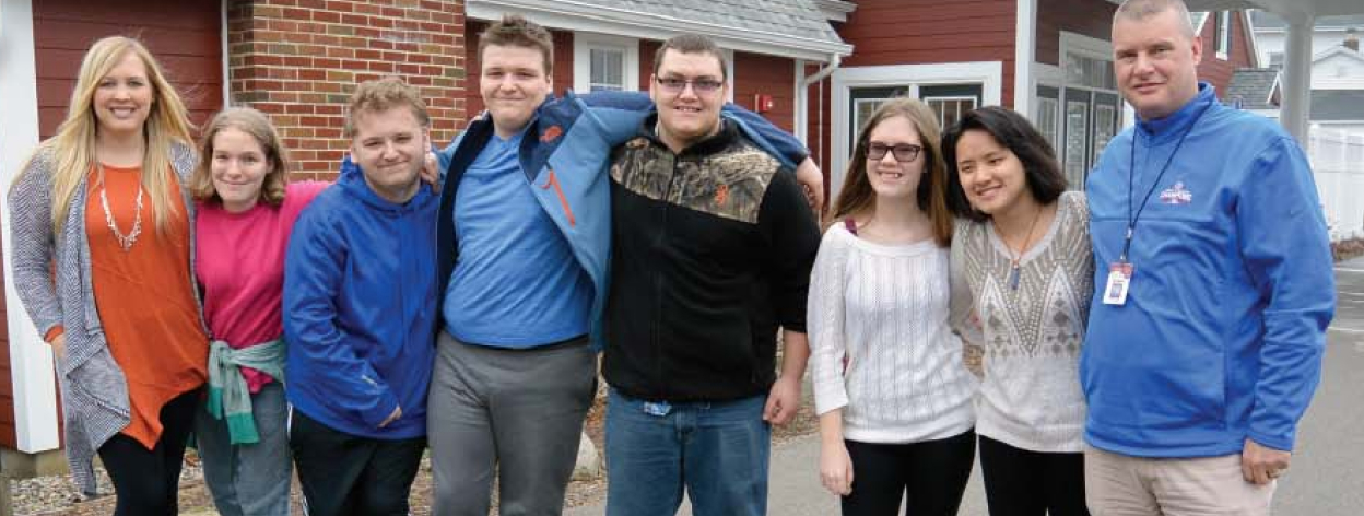 A group of young people stand in a line, shoulder to shoulder with their arms around each other.