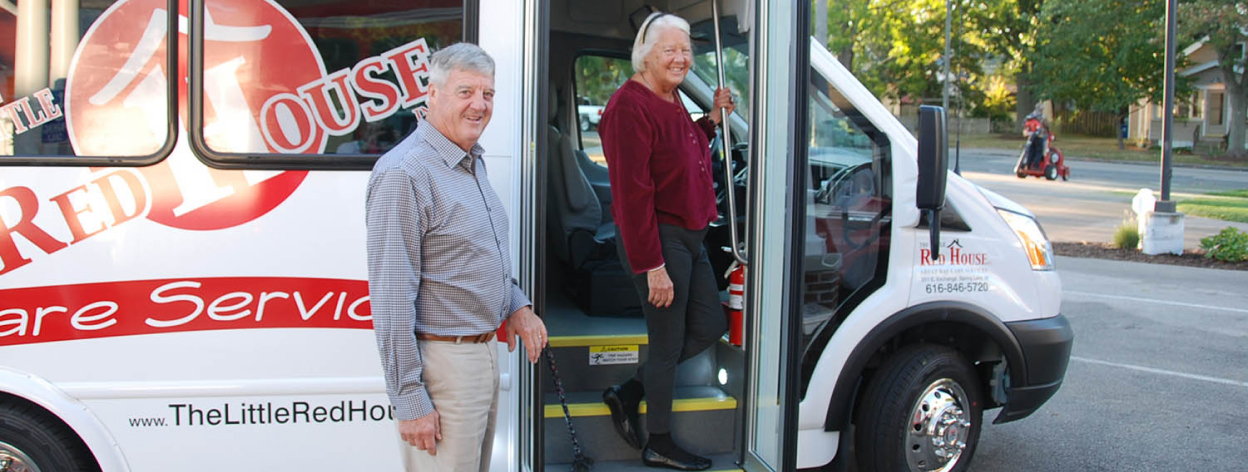A man stands in front of the door of a shuttle bus as a woman steps down from the bus.