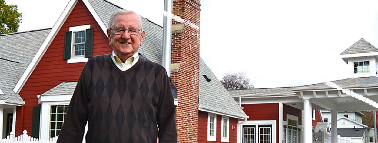 An elderly man using a cane stands in front of The Little Red House.