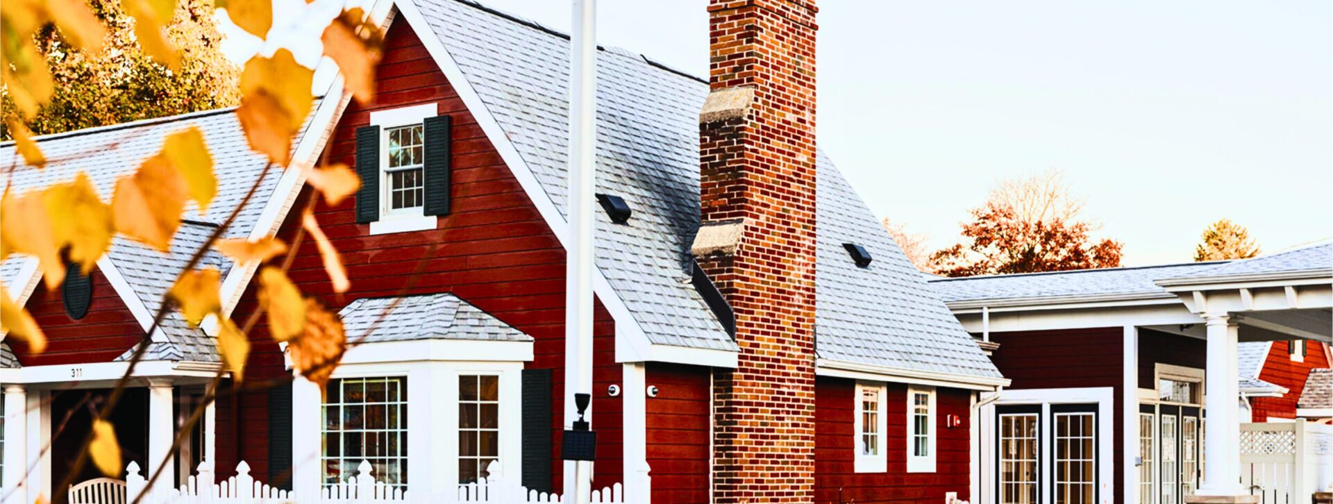 Outside of The Little Red House building showing chimney, red siding, white trim, shingles on the roof, and black shutters on the windows.